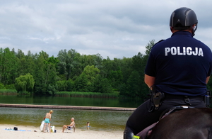 policjant nas koniu na pierwszym planie, w tle plaża i plażowicze