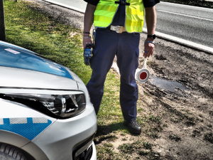policjant z ręcznym miernikiem prędkości i tarcza do zatrzymywania pojazdów stoi przy drodze na tle radiowozu
