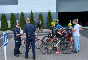 na zdjęciu stoi umundurowany funkcjonariusz i funkcjonariuszka obok na rowerach po prawej stronie stoją młode osoby z rowerami
