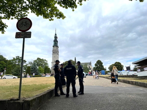 Policjanci w granatowych mundurach podczas zabezpieczenia pielgrzymki na błoniach jasnogórskich, w tle Jasna Góra i pielgrzymi