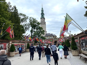 Policjanci w granatowych mundurach podczas zabezpieczenia pielgrzymki na błoniach jasnogórskich, w tle Jasna Góra i pielgrzymi