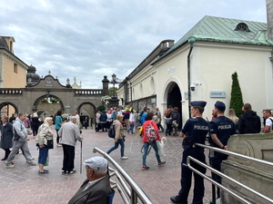 Policjanci w granatowych mundurach podczas zabezpieczenia pielgrzymki na błoniach jasnogórskich, w tle Jasna Góra i pielgrzymi