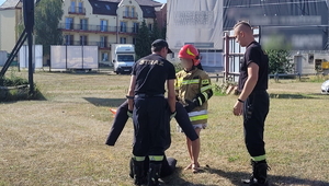 na zdjęciu kobieta ubrana w umundurowanie straży pożarnej, obok stoi dwóch strażaków z których jeden trzyma manekina
