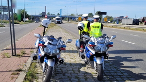 na zdjęciu stoją dwa oznakowane policyjne motocykle, obok nich stoją umundurowani policjanci