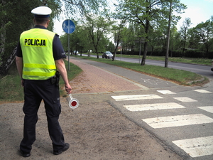 policjant z tarcza do zatrzymywania pojazdów w ręku stoi przy przejściu dla pieszych, w tle widać jadące samochody