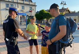 policjant w białej czapce rozdaje elementy odblaskowe pieszym