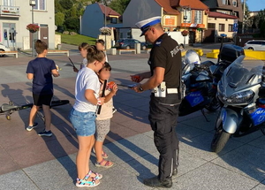 policjant w białej czapce rozdaje elementy odblaskowe pieszym