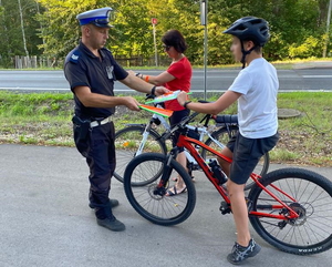 policjant ruchu drogowego w białej czapce rozdaje opaski odblaskowe rowerzystom