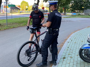 policjant ruchu drogowego w białej czapce rozdaje opaski odblaskowe rowerzystom