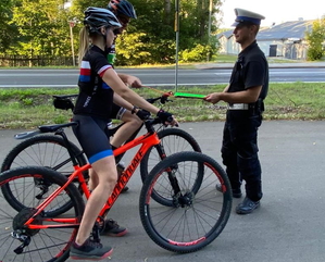 policjant ruchu drogowego w białej czapce rozdaje opaski odblaskowe rowerzystom