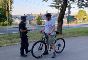 policjant ruchu drogowego w białej czapce rozdaje opaski odblaskowe rowerzystom
