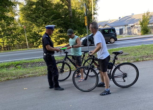 policjant ruchu drogowego w białej czapce rozdaje opaski odblaskowe rowerzystom