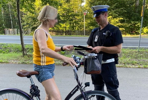 policjant ruchu drogowego w białej czapce rozdaje opaski odblaskowe rowerzystom