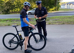 policjant ruchu drogowego w białej czapce rozdaje opaski odblaskowe rowerzystom