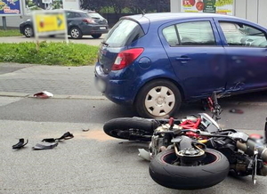 motocykl leży na jezdni obok niebieskiego samochodu marki Opel