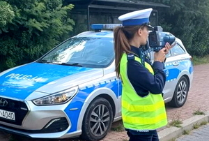 policjantka na tle radiowozu mierzy prędkość przejeżdżającym pojazdom