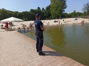 policjant stoi na pomoście - patrzy w kierunku kąpiących się w zbiorniku wodnym