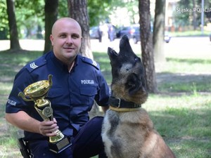 policjant trzyma w ręku puchar, obok stoi Jarika - ma uniesiony pysk do góry