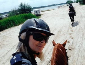 policjantka na koniu - zbliżenie na jej twarz, w tle plaża i policjant na koniu idący w kierunku zbiornika wodnego