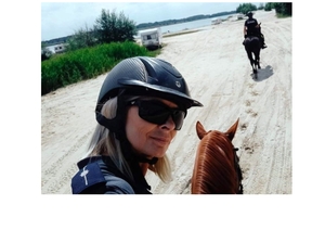 zbliżenie na twarz policjantki na koniu, w tle policjant na koniu idzie po plaży w kierunku zbiornika wodnego