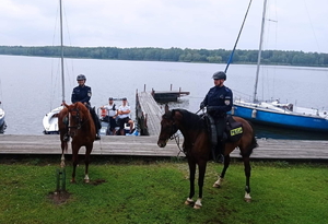 policjanci na koniach służbowych pozują do zdjęcia na tle zbiornika wodnego, w tle policjanci na łodzi policyjnej