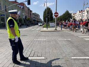 policjant na skrzyżowaniu kieruje ruchem, widać przechodzących przez przejście dla pieszych pielgrzymów