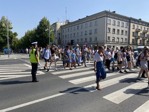 policjant na skrzyżowaniu kieruje ruchem, widać przechodzących przez przejście dla pieszych pielgrzymów