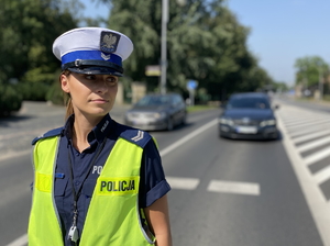 policjantka z ruchu drogowego stoi tyłem do pojazdów na skrzyżowaniu - zbliżenie na jej twarz