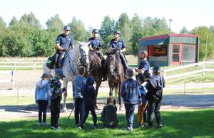 grupa dzieci stoi przy koniach służbowych na których siedzą jeźdźcy