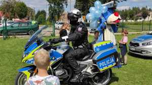 policjant na motocyklu odwraca głowę w kierunku chłopca, za policjantem stoi Sznupek - duża maskotka policyjna