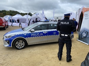 policjant stoi tyłem do fotografującego, przed nim stoi radiowóz