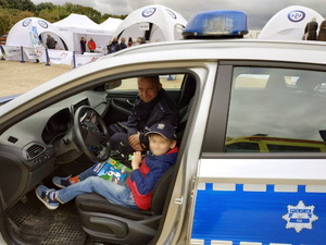 chłopiec siedzi na siedzeniu kierowcy w radiowozie, pozuje do zdjęcia, na fotelu pasażera siedzi policjant