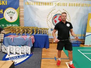 Grzegorz Maciejewski w sportowym stroju pozuje do zdjęcia na tle pucharów