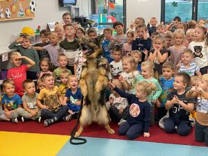 zdjęcie grupowe - pies służbowy stoi na dwóch tylnych łapach przed grupą przedszkolaków