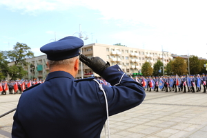 policjant oddaje honor, w tle kolumny pododdziałów policji