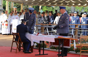 podkomisarz Rafał Jankowski podpisuje się siedząc na krześle przed stolikiem ustawionym przy ołtarzu