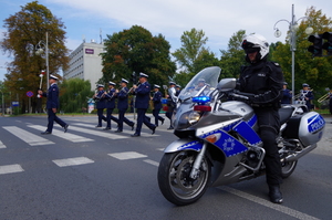 policjant na motocyklu blokuje ruch pojazdów, w tle przejście dla pieszych, po którym przechodzą policjanci