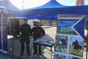 na zdjęciu umundurowani policjanci stojący przy stoliku z materiałami i ulotkami promocyjnymi