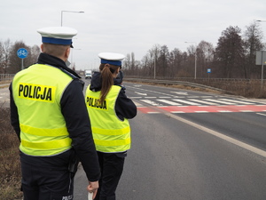 umundurowany policjant i policjantka mierzą prędkość przejeżdżających pojazdów na drodze
