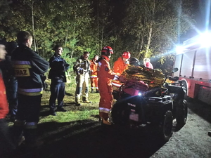 policjanci i strażacy podczas poszukiwań na terenie leśnym. Stoją wokół pojazdu typu quad