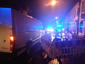 tył białego samochodu dostawczego, w tle widać niebieskie światła nadawane przez pojazdy policji i pogotowia ratunkowego - zdjęcie wykonane późnym wieczorem, jest ciemno