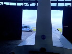 wnętrze hangaru - w środku przyczepa z wrakiem szybowca, w tle radiowóz i policjanci