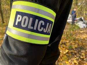 zbliżenie na opaskę naramienną z napisem policja, w tle wrak szybowca