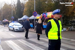 policjant w kamizelce odblaskowej stoi przy cmentarzu, w tle radiowóz