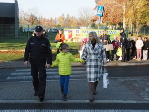 policjant i pracownica Starostwa przeprowadzają przez jezdnię za rękę ucznia