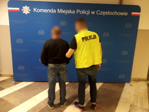 policjant w kamizelce odblaskowej trzyma pod ramię zatrzymanego na korytarzu Komendy w Czestochowie