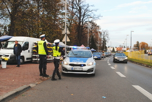 policjantka i policjant stoją przed radiowozem w rejonie cmentarza