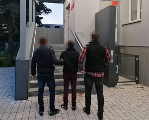 dwóch nieumundurowanych policjantów prowadzi zatrzymaną kobietę pod ręce do wejścia do komisariatu w Warszawie