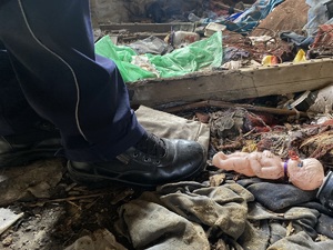 nas zdjęciu zbliżenie na buta policjanta, obok nas ziemi lalka i śmieci - policjant kontroluje pustostan