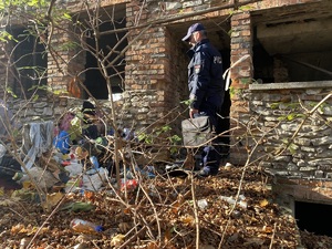 na zdjęciu policjant z teczką wchodzi do opuszczonego budynku, przed wejściem znajduje się mnóstwo śmieci